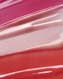 Macro shot of glossy cosmetic lip gloss swatches in shades of pink, white, and red with a smooth texture