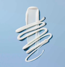 White cosmetic cream smeared and swirled in abstract lines on a solid light blue background.