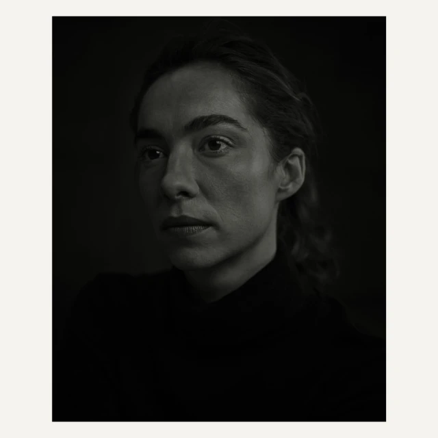 Monochrome portrait of a woman with dark hair in a black turtleneck against a dark background, emphasizing light and shadow.