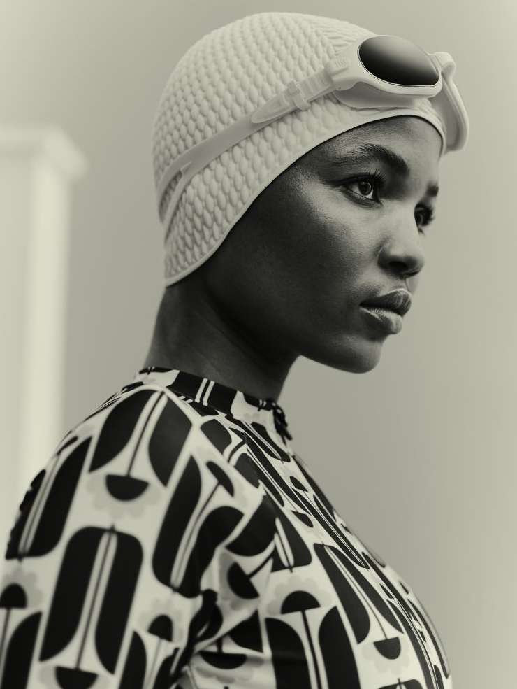 Monochrome portrait of an African American woman wearing a patterned swimsuit and swim cap with goggles, looking to the side.
