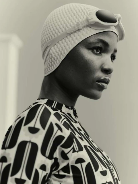 Monochrome portrait of an African American woman wearing a patterned swimsuit and swim cap with goggles, looking to the side.