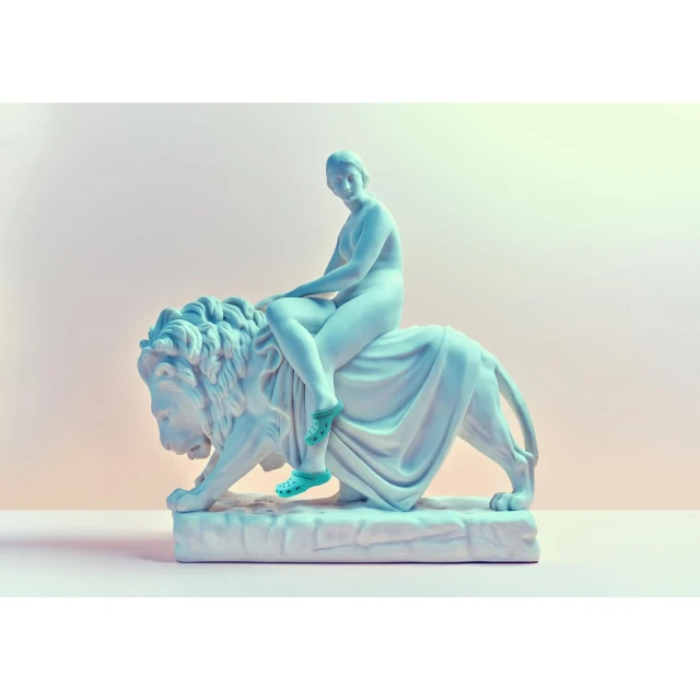 Statue of nude female figure riding a lion, both made of stone, posed against a plain light background in an indoor setting.