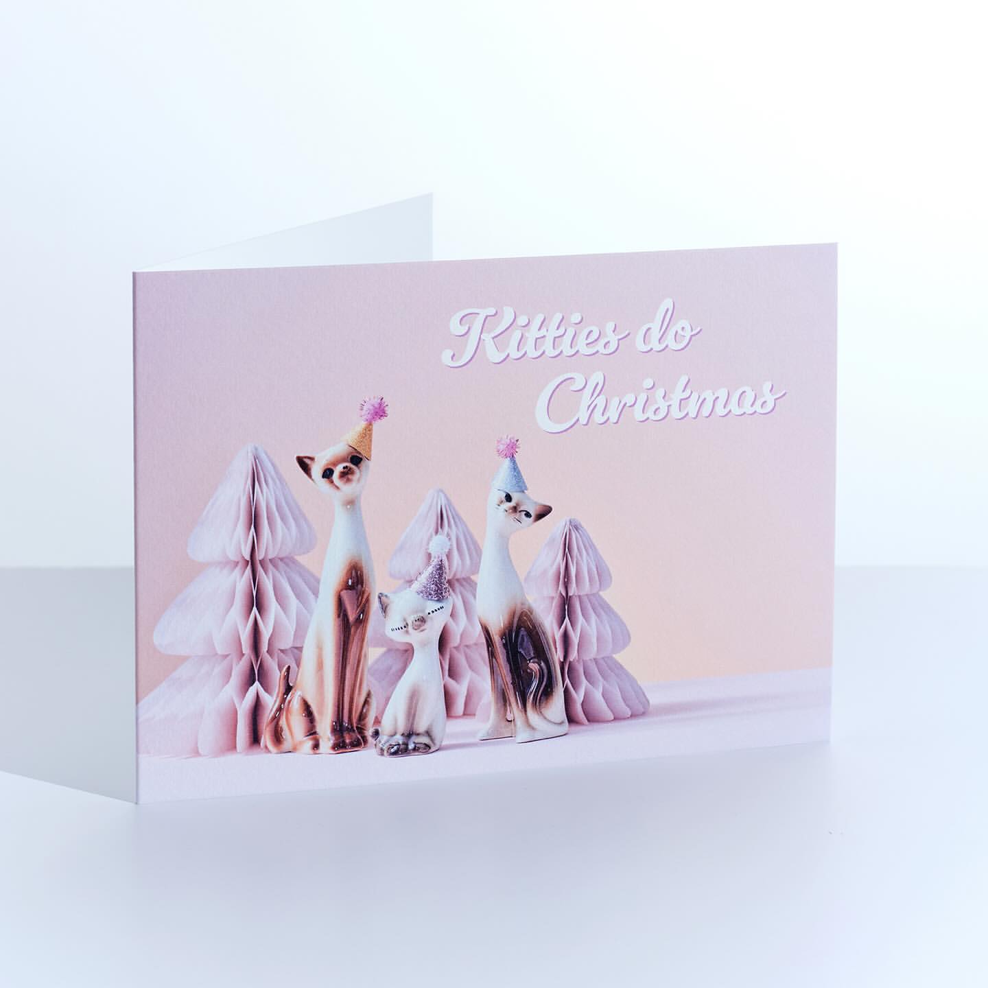 Whimsical holiday card featuring stylized animal figures wearing festive hats amidst honeycomb paper Christmas trees, soft lighting, and joyful aesthetic.