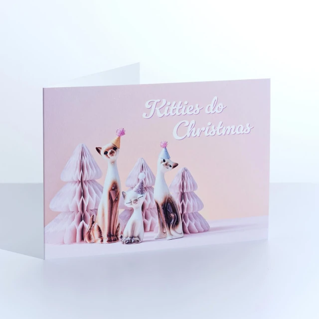 Whimsical holiday card featuring stylized animal figures wearing festive hats amidst honeycomb paper Christmas trees, soft lighting, and joyful aesthetic.