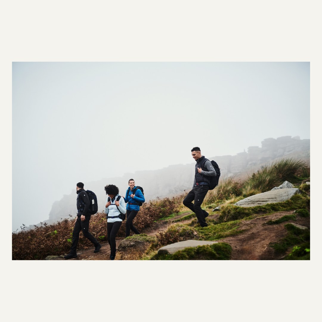 Group of four people with backpacks hiking on a grassy hillside on a foggy day. Outdoor adventure and travel photography.