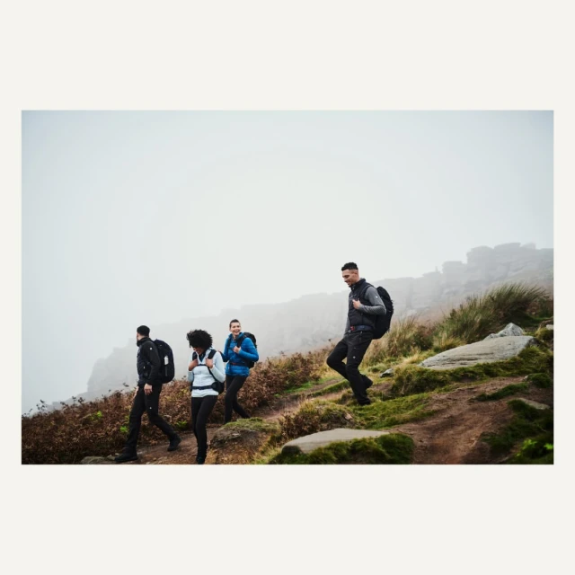 Group of four people with backpacks hiking on a grassy hillside on a foggy day. Outdoor adventure and travel photography.