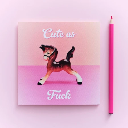 Quirky still life with a toy horse on a square card with pink hues, accompanied by a pink colored pencil.