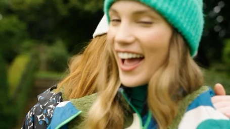 Two smiling women in winter beanies and outerwear embracing outdoors in a park