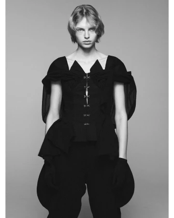 Monochrome portrait of a model in a dark structured top with sheer sleeves and gloves against a neutral grey background.