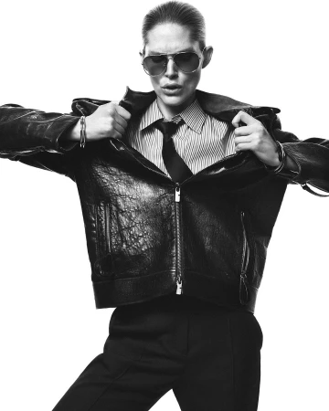 Model in aviator sunglasses wearing a black leather jacket over a striped shirt and tie against a white background.