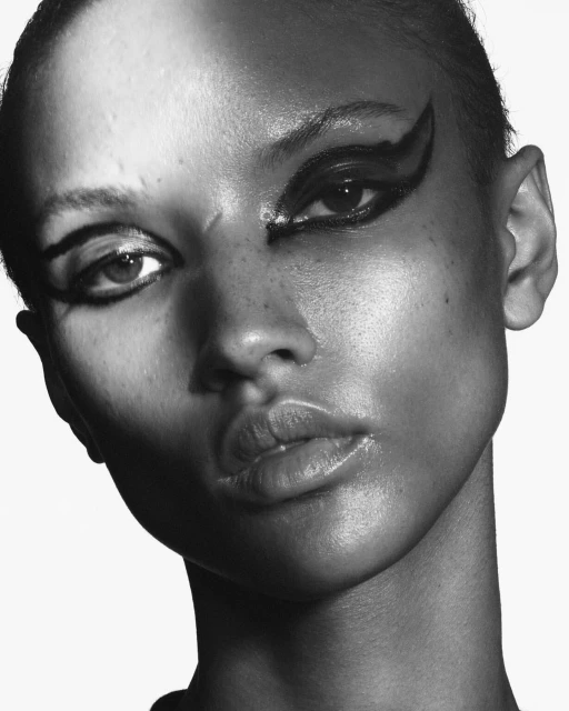 Striking black and white portrait of a woman with graphic black eye makeup, showcasing beauty and fashion in a high-contrast close-up.