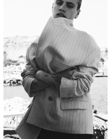 Model with short hair wearing an oversized striped blazer with arms crossed outdoors by water