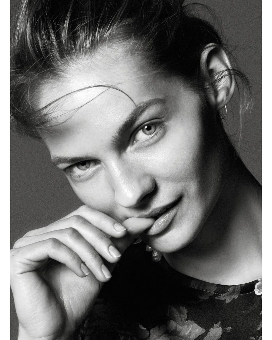 Monochrome close-up portrait of a woman with updo hairstyle, floral patterned top, and soft diffused lighting in a photo studio.