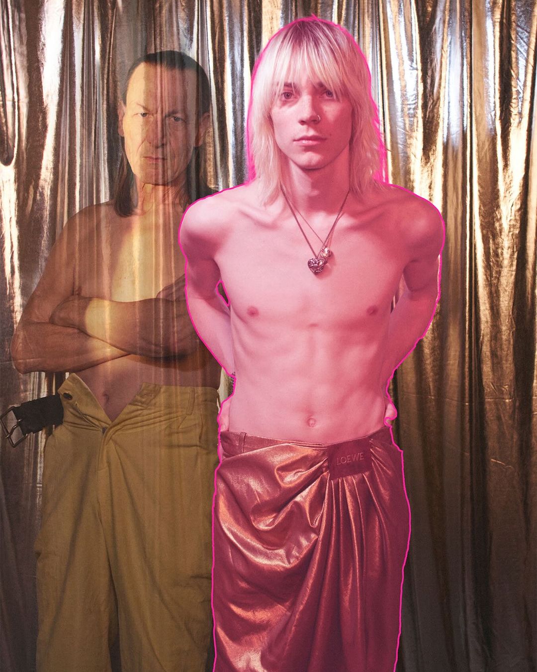 Two men in front of a textured backdrop. One man stands in the foreground in a wrap skirt, while the other is superimposed behind.