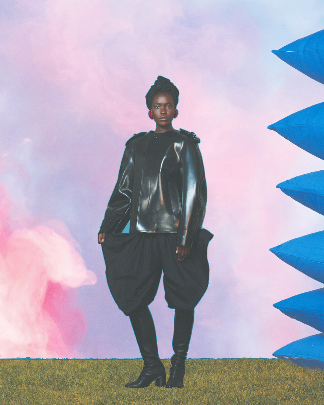 A tall, slender, Black female model in a black leather jacket, black puffy shorts, leggings, and high-heeled boots is in a fashion shot.