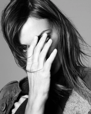 Close-up monochrome portrait of a woman holding her hand across her face with hair falling past her eyes by David Sims.