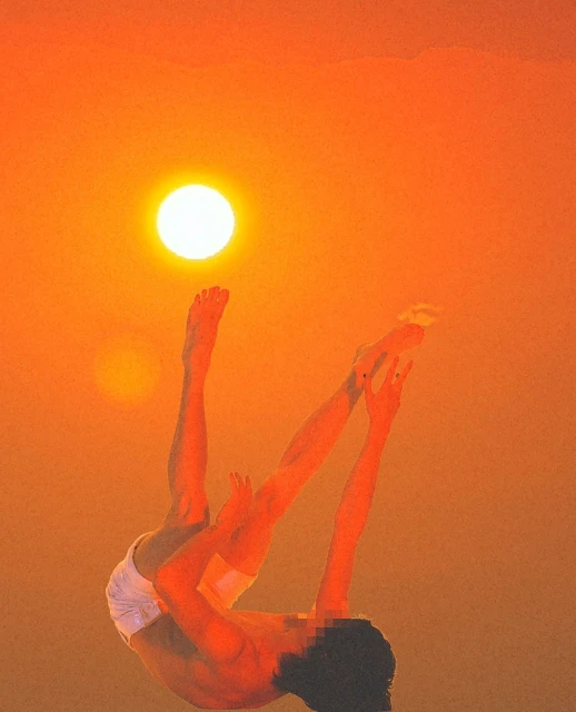 Artistic image of a shirtless man against a blurred orange sky and suns. Inverted pose with head blurred out and legs in the air.