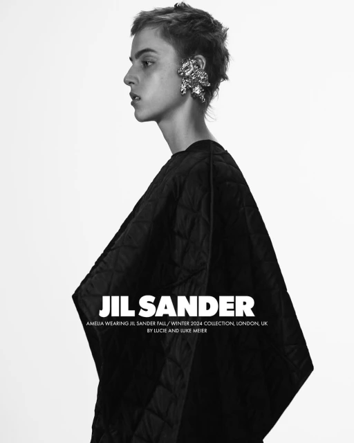 Black-and-white portrait of a female fashion model in a dark quilted poncho, facing left, and wearing a large silver earring.