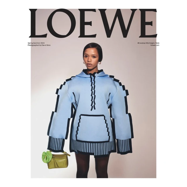 Fashion editorial featuring a woman in a light blue hoodie and a green bag, posing against a neutral backdrop with brand text overhead.