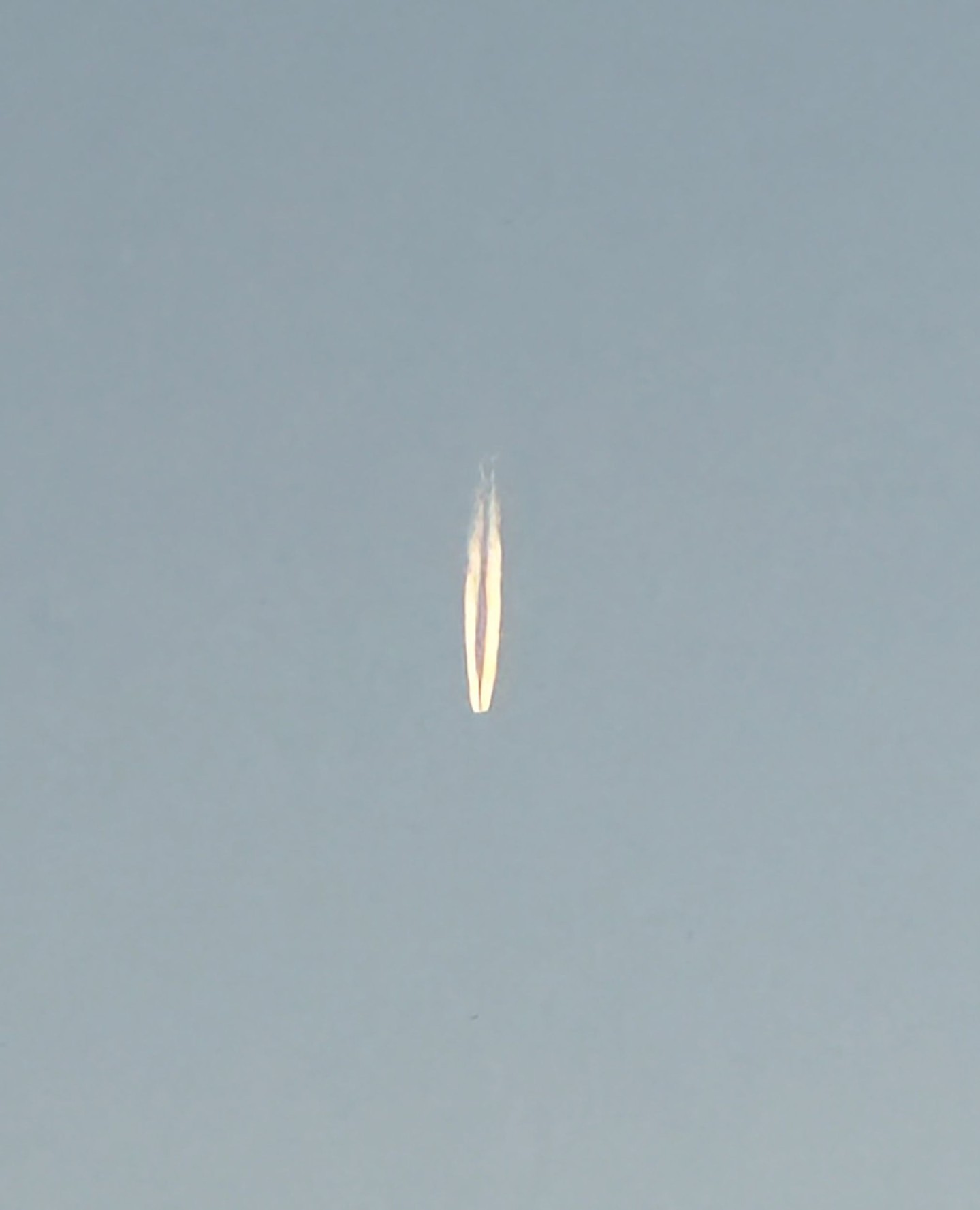A vapor trail from a plane stretches across the blue sky, creating a long, symmetrical line with a hazy effect, dominating the image.