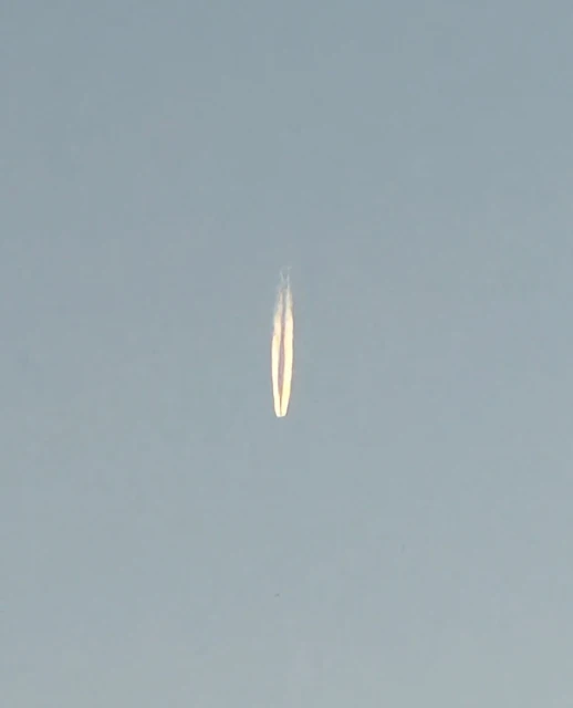 A vapor trail from a plane stretches across the blue sky, creating a long, symmetrical line with a hazy effect, dominating the image.
