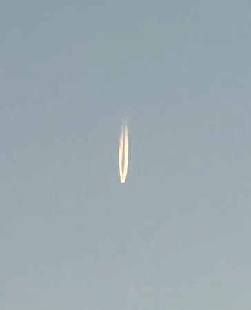 A vapor trail from a plane stretches across the blue sky, creating a long, symmetrical line with a hazy effect, dominating the image.