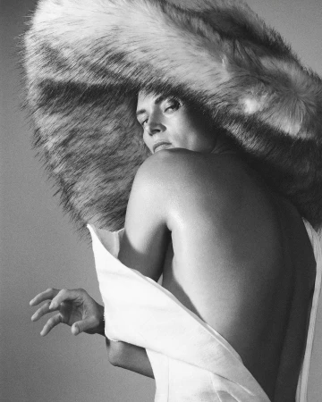 Model wearing an oversized furry hat and white garment looking over shoulder, photographed by David Sims.