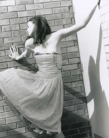 Black and white editorial photo of a woman in a strapless dress pressing against a brick wall by David Sims