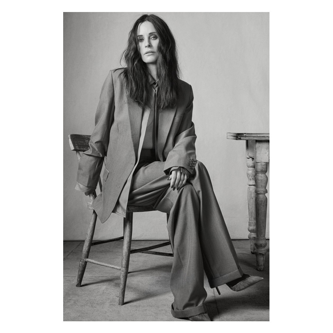 Monochrome portrait of a woman seated on a wooden chair wearing an oversized suit