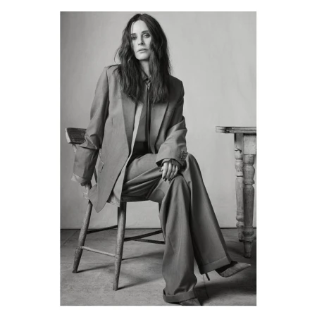 Monochrome portrait of a woman seated on a wooden chair wearing an oversized suit
