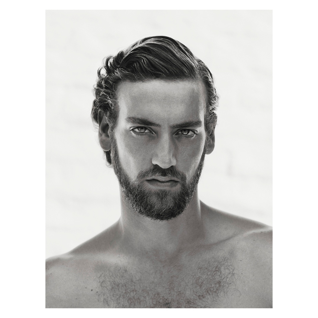 Portrait of a man with dark styled hair and a trimmed beard against a plain background