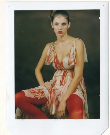 Model seated wearing a patterned dress and red tights inside a white polaroid frame by David Slijper