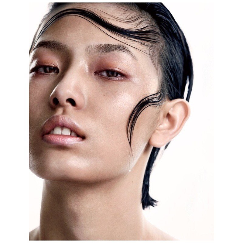 Close-up portrait of a woman with wet dark hair strands slicked across her forehead against a plain white background