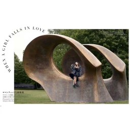 Model seated inside a large curved bronze outdoor sculpture wearing a dark puffer jacket over a black dress on a grassy lawn.