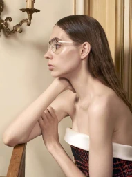 Profile portrait of a woman wearing wire-rimmed glasses and a strapless tweed dress against an off-white wall by David Slijper