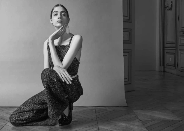 Model in a dark textured matching top and trousers kneeling on a parquet floor in a studio setting
