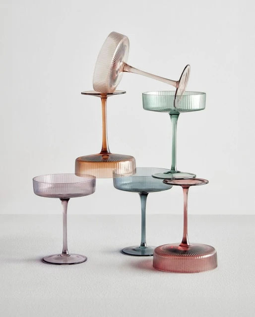 Elegant composition of stacked ribbed coupe glasses in pastel colors against a light backdrop, creating a sophisticated drinkware arrangement.