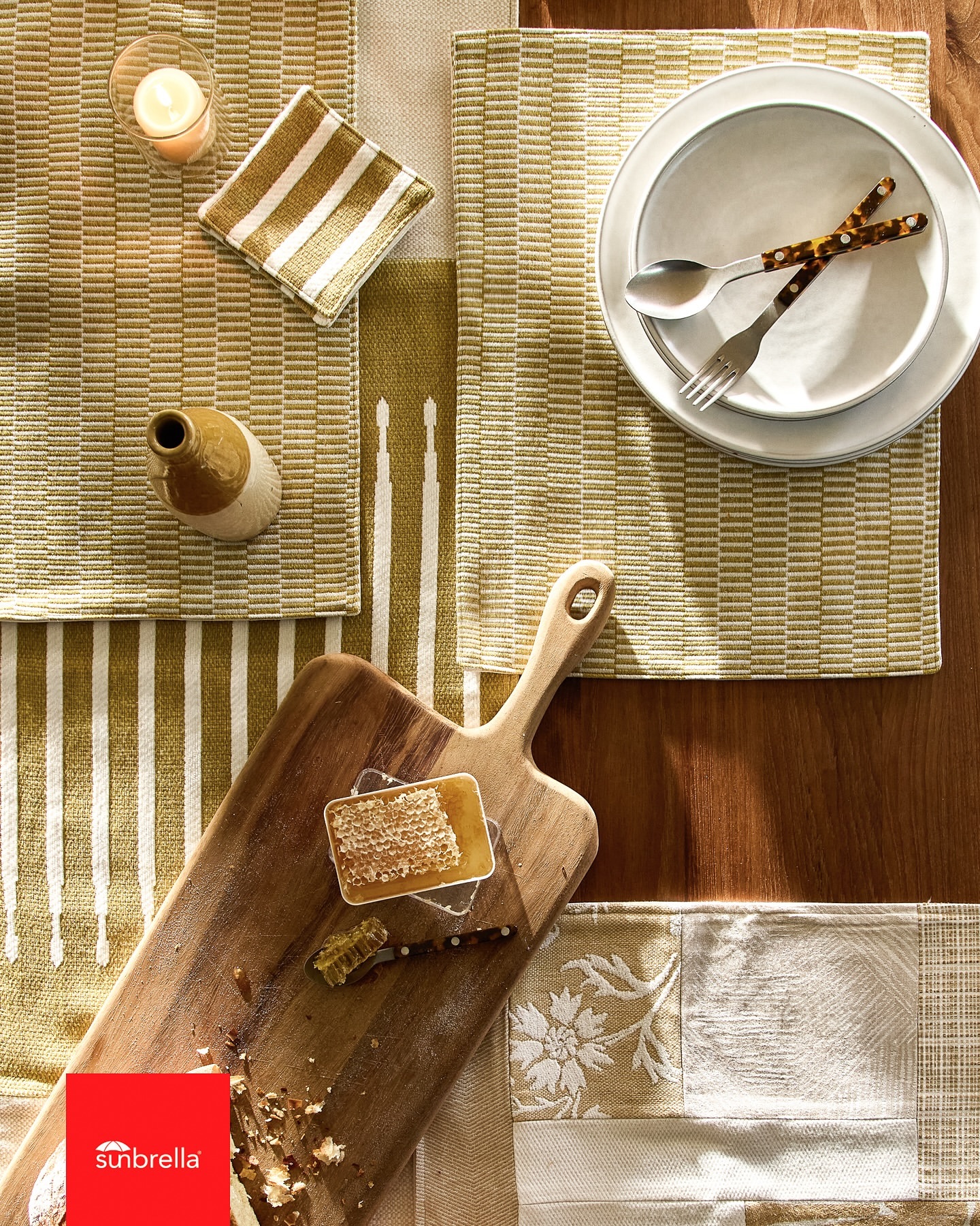 Overhead shot of elegant tableware, silverware, honeycomb, and textiles in earth tones, arranged on a wooden surface with natural light.