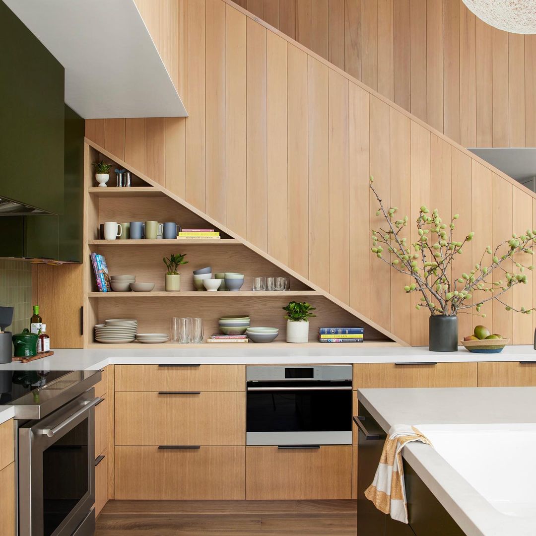 Interior shot of a modern kitchen with wood cabinets, white countertops, built-in shelving, and decorative house plants in vases.