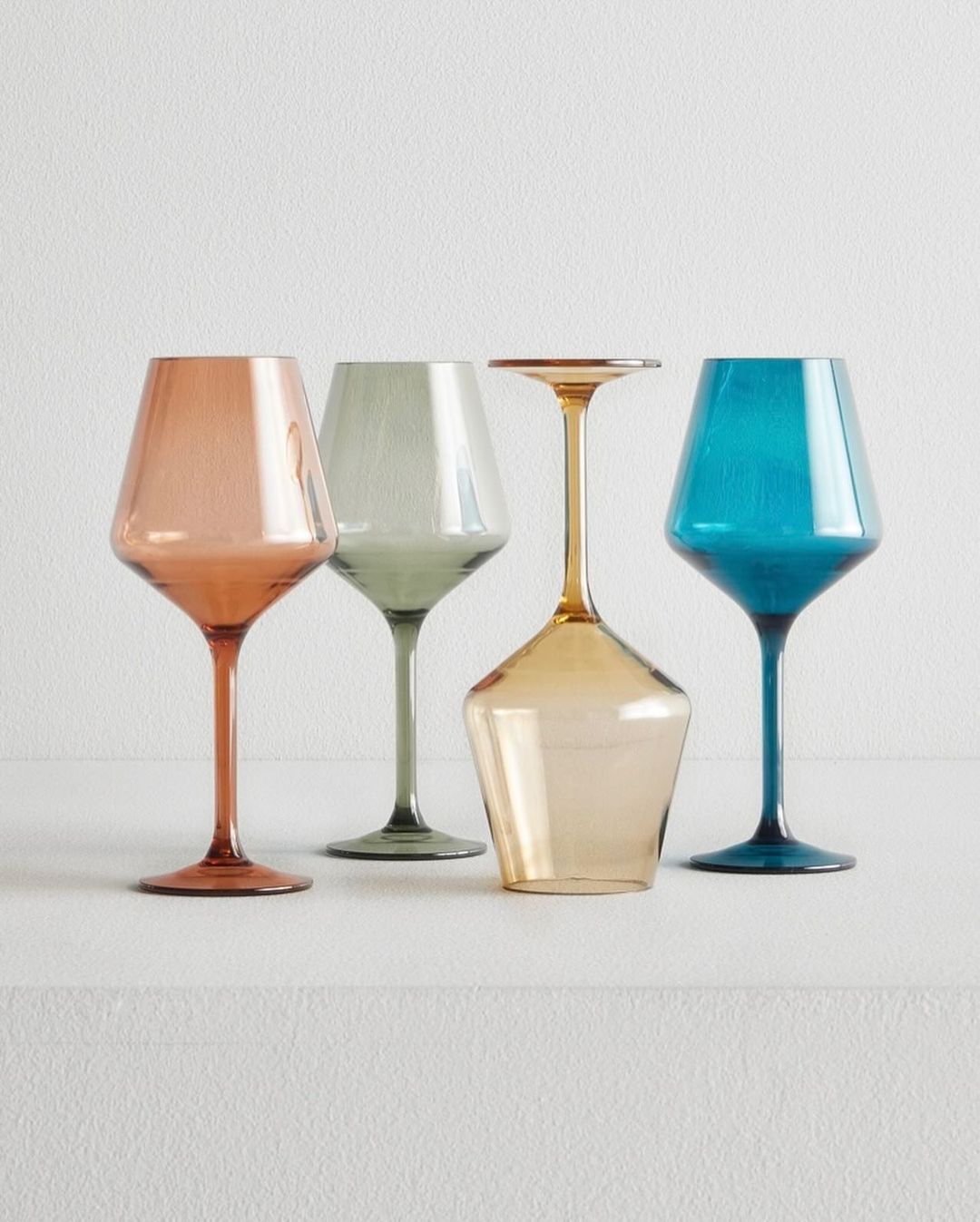 Four colorful, stemmed wine glasses in a row, featuring shades of amber, green, and blue, against a plain white background.
