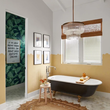 Bathroom interior with a black clawfoot tub, round jute rug, and white walls with gold scalloped trim, lit by a tiered chandelier.