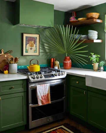 Green kitchen interior featuring a stainless steel oven, yellow teapot, and decor elements such as a vase, plant, and wall art.