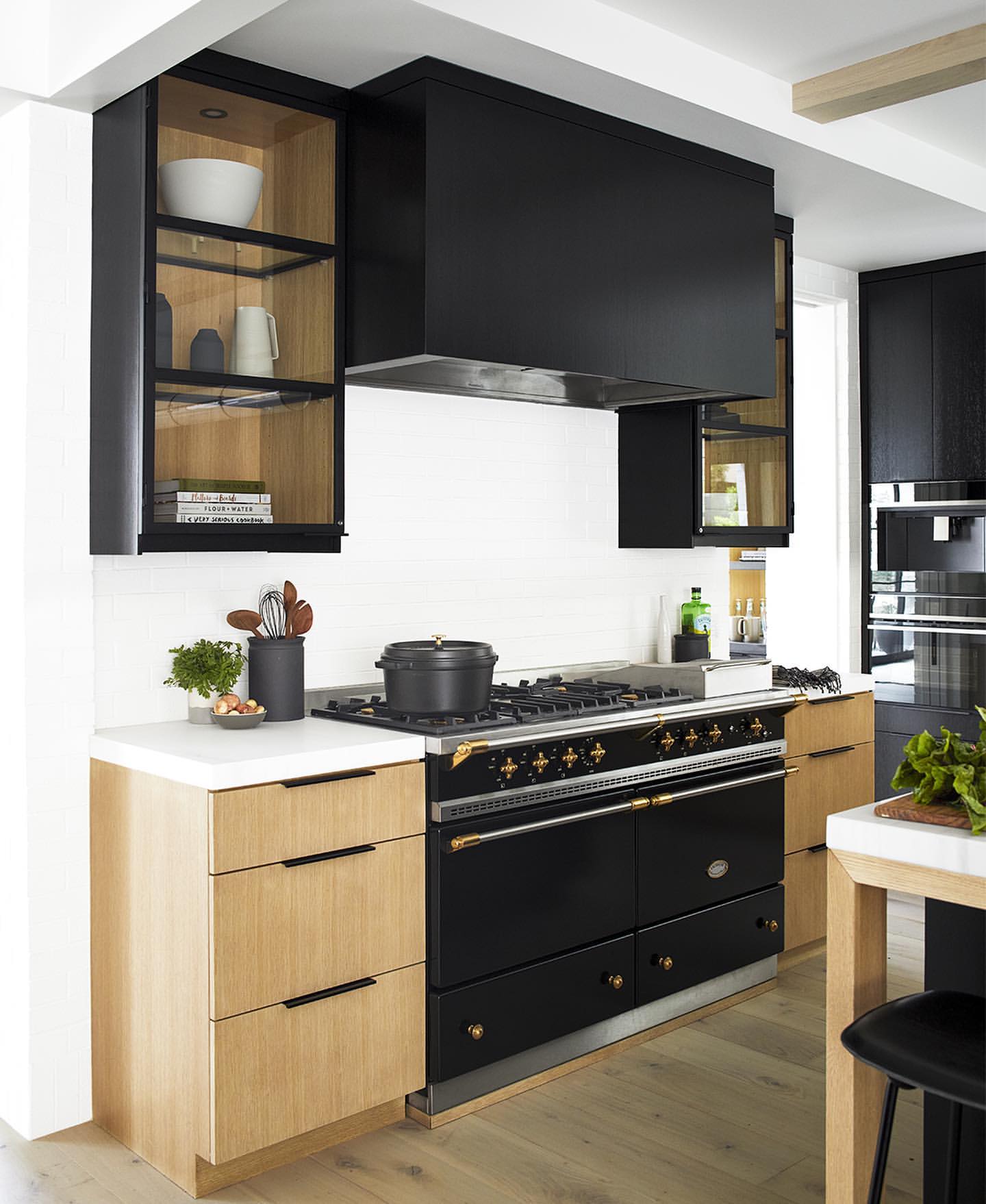 Modern kitchen interior with a black range cooker, light wood cabinets, and white countertops, under a black range hood.