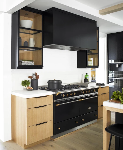 Modern kitchen interior with a black range cooker, light wood cabinets, and white countertops, under a black range hood.
