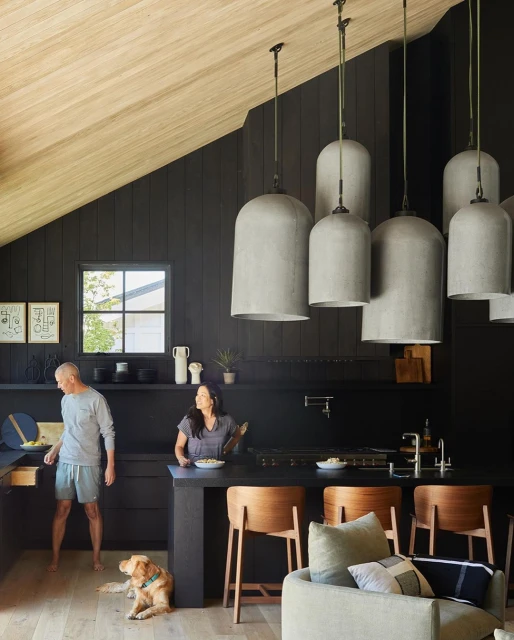 Contemporary black kitchen with two adults, a golden retriever, pendant lights, wood accents, and architectural elements.
