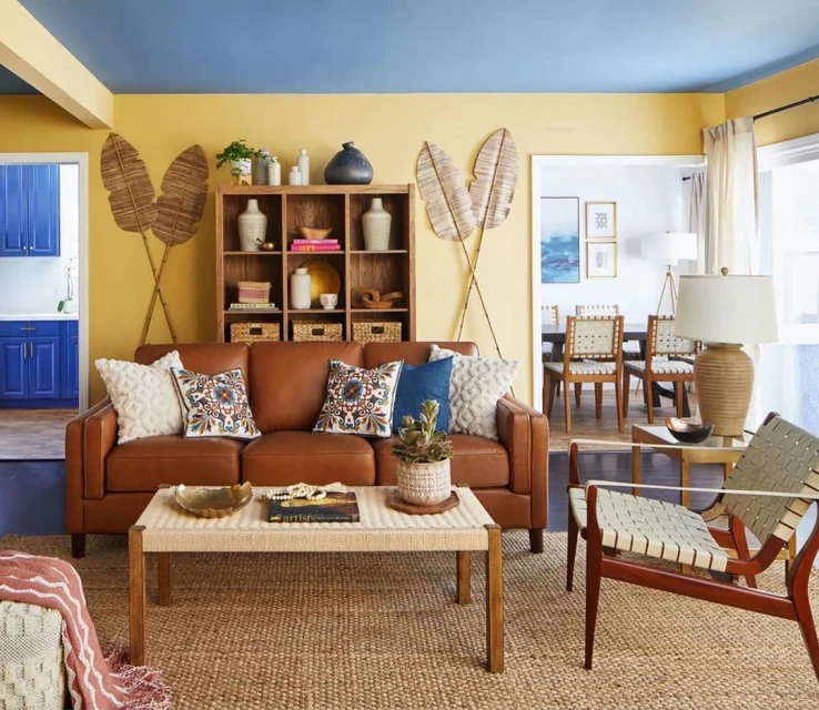 Living room with a brown leather sofa with decorative pillows, a light brown coffee table, and two chairs in a naturally lit space.