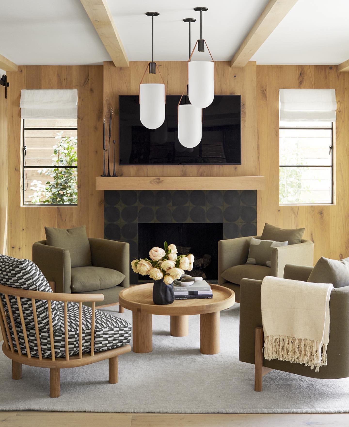 Cozy living room features four armchairs, a round coffee table, modern pendant lighting, and a fireplace with a wall-mounted TV.