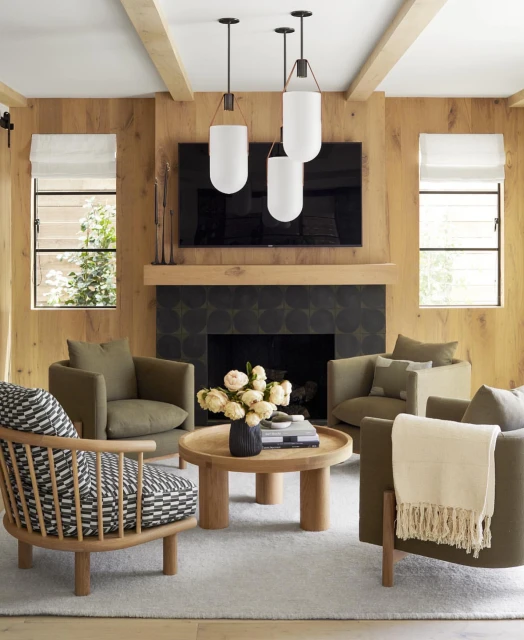 Cozy living room features four armchairs, a round coffee table, modern pendant lighting, and a fireplace with a wall-mounted TV.