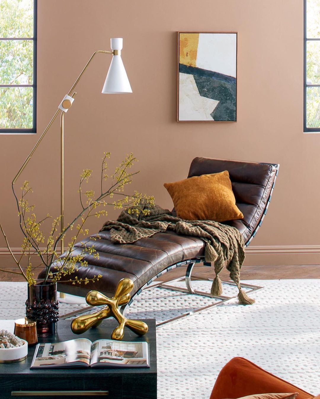 Living room setup featuring a brown leather chaise lounge with a throw pillow, a modern floor lamp, and decorative objects on a coffee table.