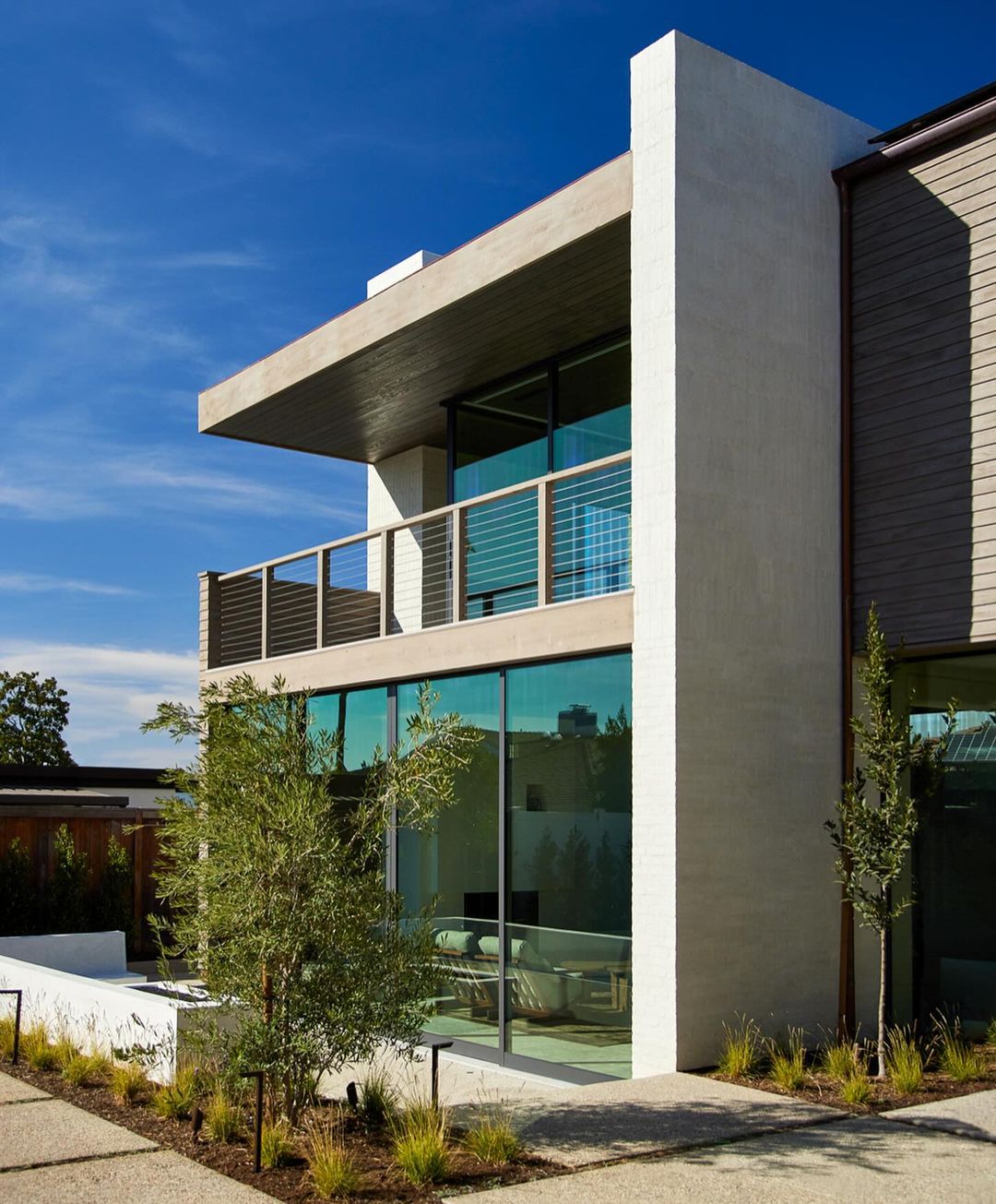 Exterior of a modern house with large glass windows and a balcony on a sunny day, showcasing contemporary architecture.